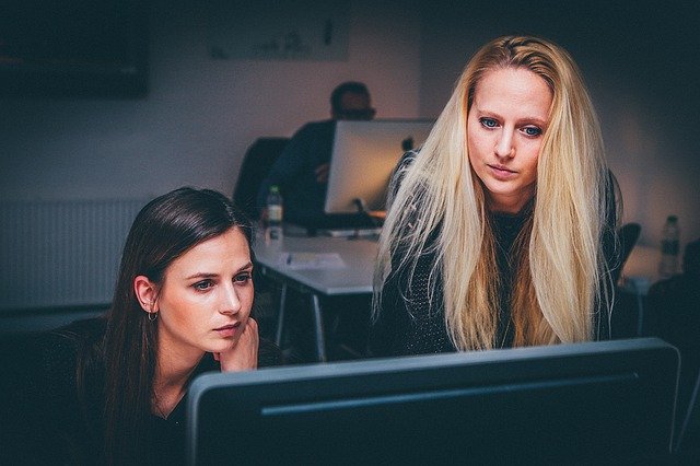 Image of two women with one stood looking at a computer screen on starting a business as an international student